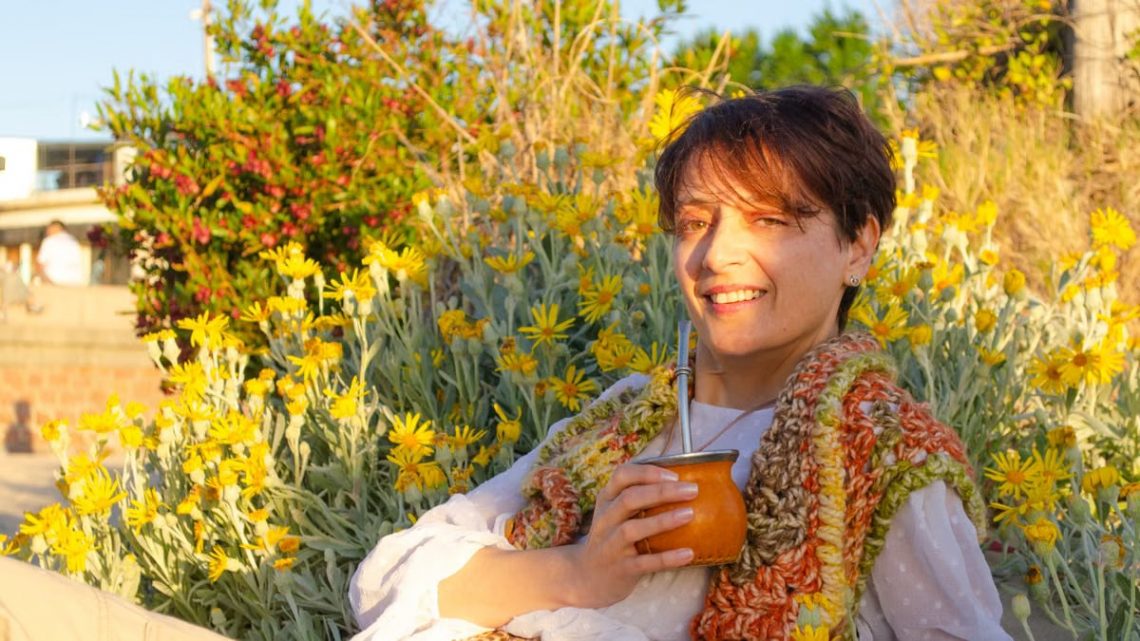 A woman smiles while drinking traditional mate among yellow flowers in Montevideo.
