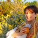 A woman smiles while drinking traditional mate among yellow flowers in Montevideo.