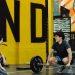 Two young adults in a gym participating in a weightlifting session, sharing a positive moment.